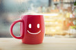 © eddows - Red mug of coffee with a happy smile, Steaming red coffee cup on a rainy day window background, Good morning or have a happy day message concept