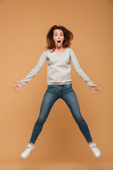 Poster - Full length photo of shocked young woman in gray blouse and jeans jumping over beige background