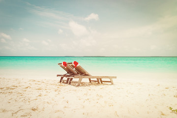 Wall Mural - Christmas on beach -chair lounges with Santa hats at sea