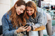 © Drobot Dean - Two charming woman friends looking at mobile phone while sitting in cafeteria