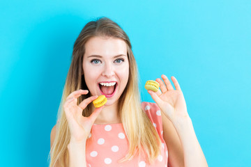 Wall Mural - Happy young woman holding macarons on a blue background