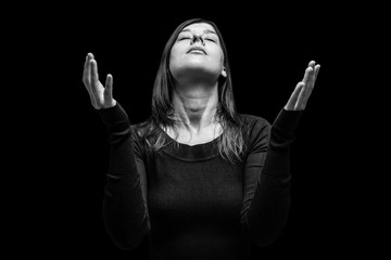 Mourning woman praying, with arms outstretched in worship to god, head up and eyes closed in suffer, on black background. Concept for religion, faith, prayer, grief, mourn, pain, depression.