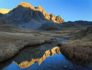 Fototapete - Mountain peaks refelcted in a small stream during an autumn sunset.