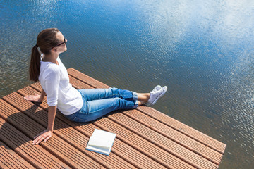 Wall Mural - People relaxing outdoors Young woman relaxing on wooden lake dock with a open book by her side. 