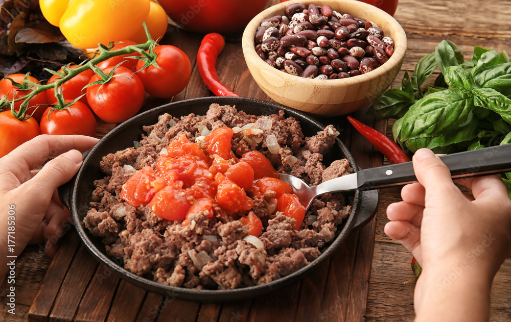 Woman adding tomato sauce to cooked minced meat in kitchen