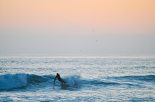 Person Surfing Alone On Ocean Waves At Sunset