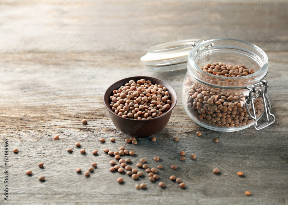 Jar and bowl with brown lentils on wooden table
