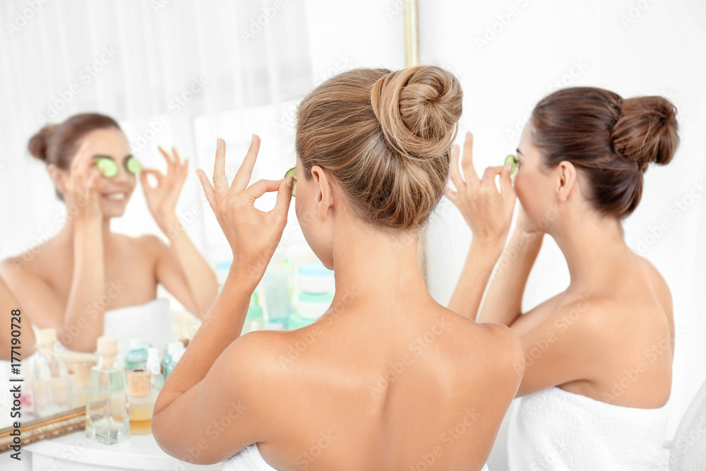 Young women with cucumber slices in bathroom