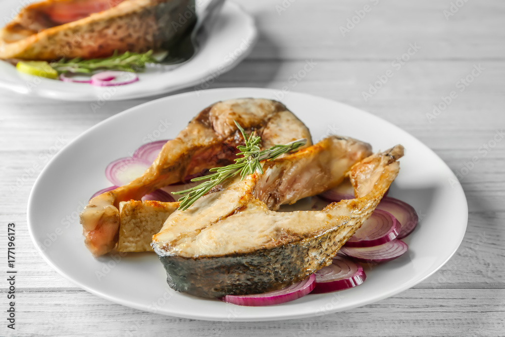 Ceramic plate with fried fish steaks on wooden background