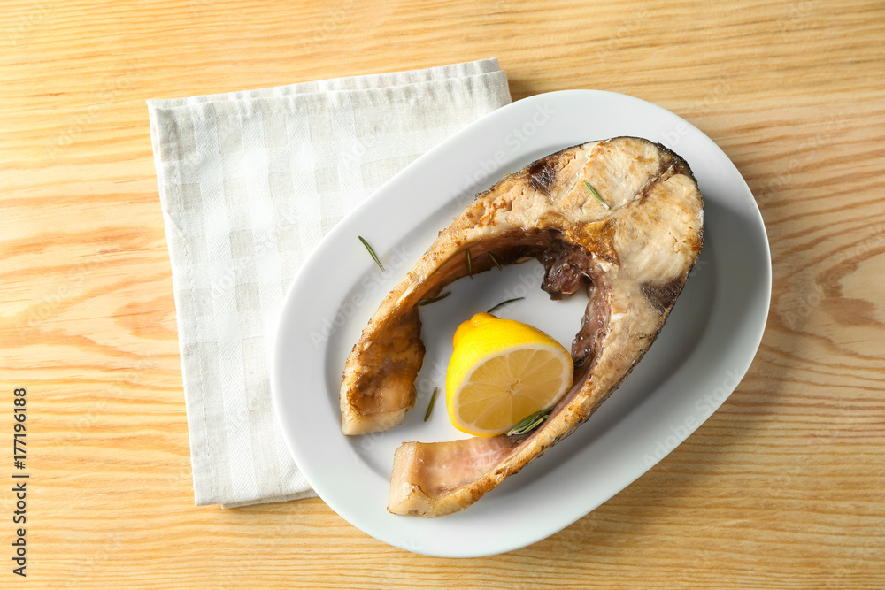 Ceramic plate with fried fish steak on wooden background