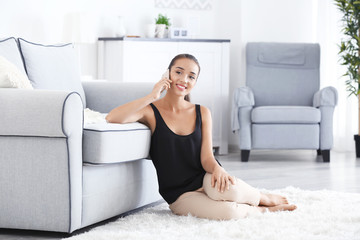 Wall Mural - Beautiful young woman speaking by mobile phone at home