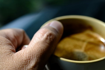 the skin of the thumb of a man's hand holding a cup of coffee.