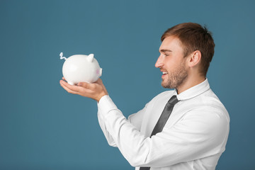 Canvas Print - Young man with piggy bank on color background