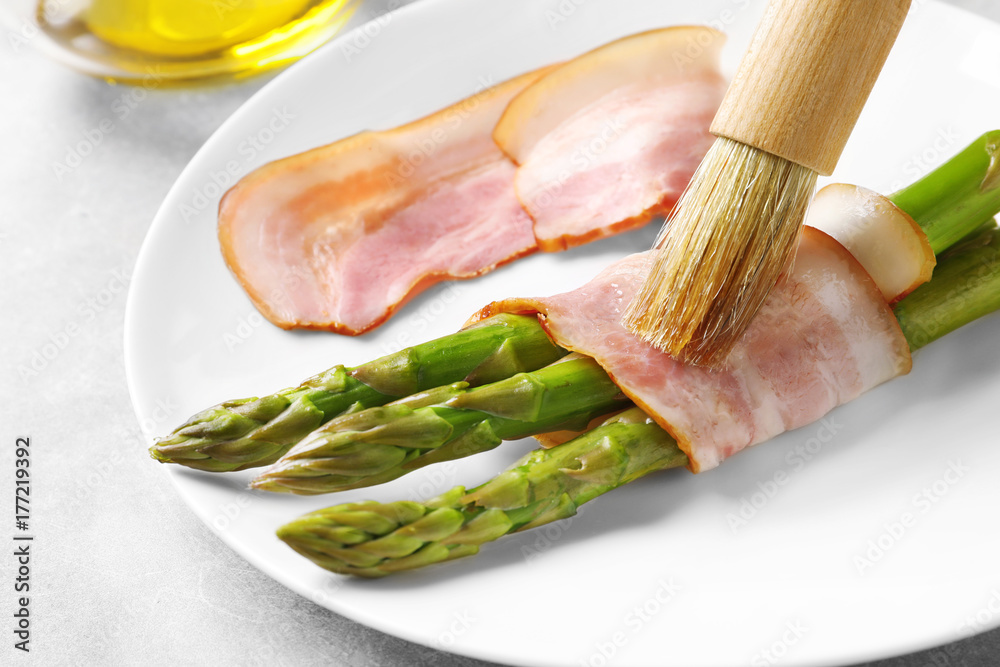Plate with bacon wrapped asparagus on light background