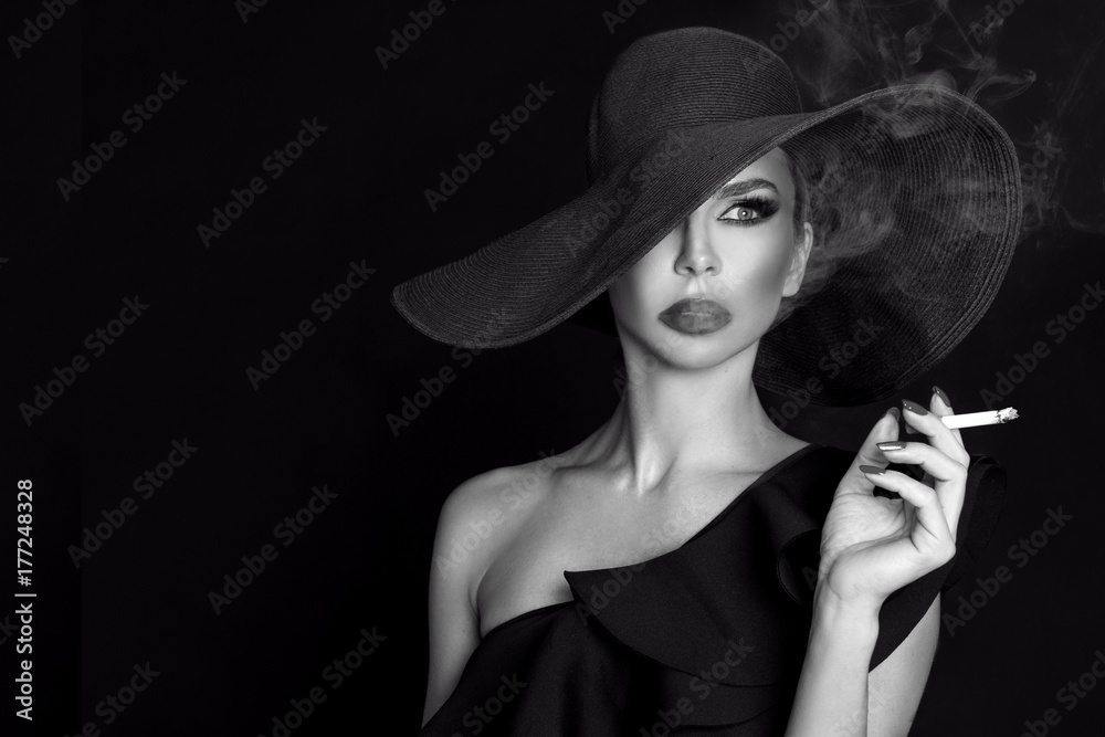 Elegant woman, femme fatale in black hat with cigarette in hand. On black  background Stock Photo