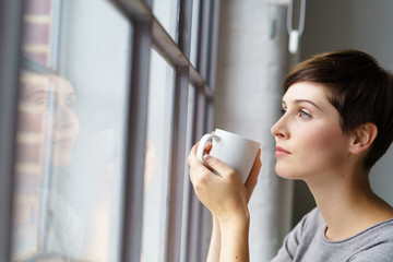 Wall Mural - frau schaut nachdenklich aus dem fenster mit einer tasse tee