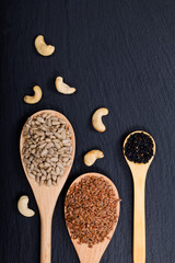 Wall Mural - Organic sunflower seeds, Flax seeds and sesame in wooden spoon and raw Cashew nuts black slate stone background with copy space