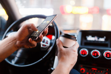 The young man makes a picture by mobile phone a Cup of coffee for social networking or a photo-sharing app. Sitting behind the wheel of a modern stylish machine in the Parking lot.