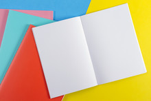 Open Notebook And Colorful Notebooks On Blue And Yellow Background