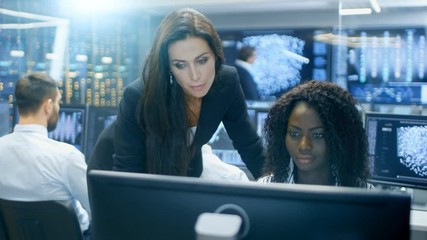 Fototapete - Female Team Leader Consults Young Computer Engineer. They Work in a Crowded Office on a Neural Network/ Artificial Intelligence Project. 