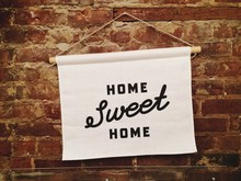 A Home Sweet Home Sign Hanging On A Brick Wall, With Handwritten Type
