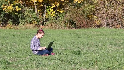 Wall Mural - happy little girl playing laptop in the park autumn season