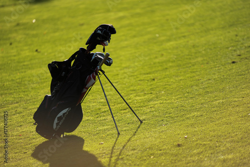 Plakat Torba golfowa stoi na polu golfowym o zachodzie słońca.