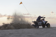 A Woman Riding A Quad And Kicking Up Sand