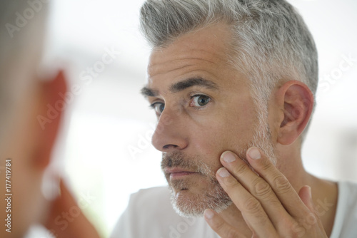 Fotografie, Obraz Middle-aged man applying cosmetic on his face, mirror view