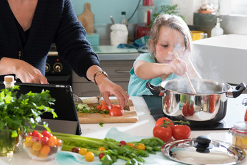 Wall Mural - A little girl cooking a recipe in the kitchen with her mother