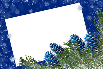 Wall Mural - Snow-covered fir branches and blue-colored cones on blue background with snowflakes and copy space on white blank sheet.