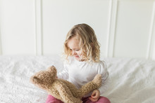 Young Girl Wearing Red And White Striped Pajamas Looks At Teddy Bear