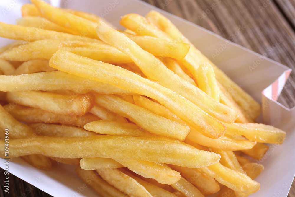 Paper container with yummy french fries on table, closeup