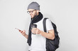 © Yulia - Handsome young European or American male tourist wearing hat, trendy shades smiling happily while reading sms on smart phone, messaging his girlfriend online using free wi-fi, having coffee take away.