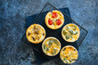 Set of savory mini tarts. Vegetable quiches with tomatoes, mushrooms, herbs, broccoli. Blue stone background.
