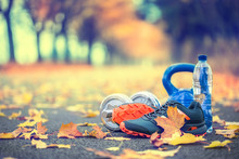 Pair Of Blue Sport Shoes Water And  Dumbbells Laid On A Path In A Tree Autumn Alley With Maple Leaves -  Accessories For Run Exercise Or Workout Activity