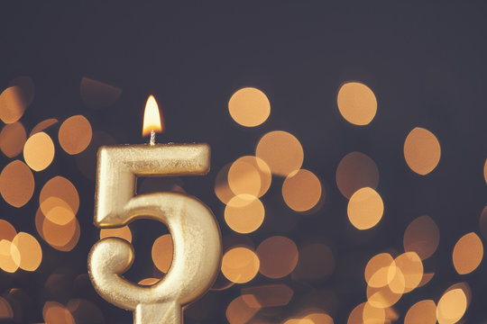 Gold number 5 celebration candle against blurred light background