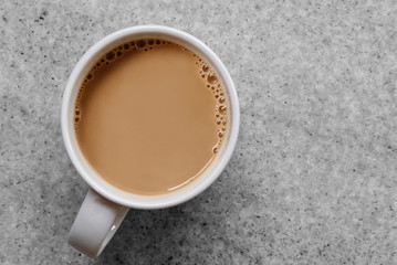 white coffee or tea with bubbles in white ceramic mug isolated on grey granite table from above.