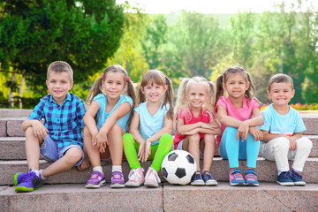 Wall Mural - Cute little children with ball sitting on stairs in city park