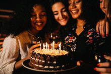Young Woman Holding A Birthday Cake, Making Wish While Friends Look On