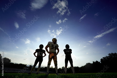 Plakat Gracze w futbol amerykański są na polu przeciw niebu o zachodzie słońca.