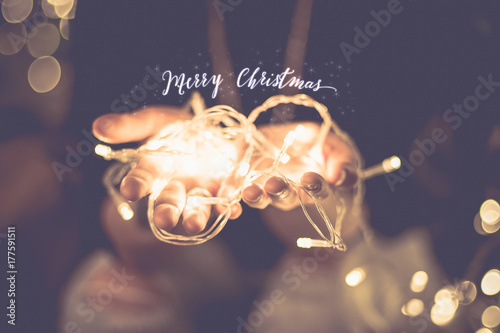 Fotomural Merry christmas glowing word over hand with party light string bokeh in vintage filter,Holiday, new year season
