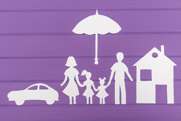 The silhouettes cut out of paper of man and woman with two girls under the umbrella, house and car near