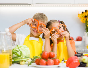 Happy kids having fun with food vegetables at kitchen holds pepper before his eyes like in glasses