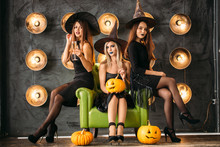 Three Happy Young Women In Black Witch Halloween Costumes On Party