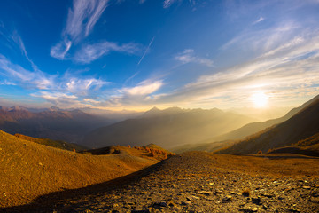 Wall Mural - The Italian French Alps at sunset. Colorful sky over the majestic mountain peaks, dry barren terrain and green valleys. Sunburst and backlight expansive view from above.