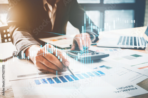 Fotomural Close up Businessman hand holding pen and pointing at finance paperwork and using calculator for do math on wooden desk at office