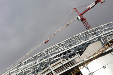 Construction crane against the gray sky. The red and white mechanism is illuminated by the sun.Diagonal placement in the frame of a construction crane and metal structures