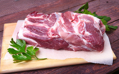 Raw pork neck chop meat with parsley herb leaves on a stone background. Ready for cooking.