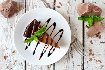 Poster - Slice of chocolate cheesecake on plate, above view over a rustic white wood background